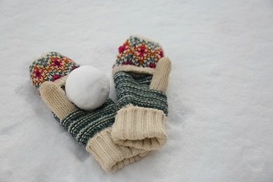 Knitted mittens and snowball on snow outdoors Photo of Knitted mittens and snowball on snow outdoors