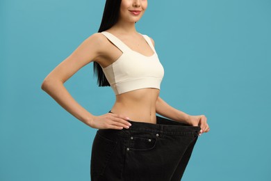 Young woman wearing big jeans after weight loss on turquoise background, closeup Photo of Young woman wearing big jeans after weight loss on turquoise background, closeup