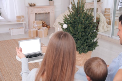 Family with child using video chat on laptop in room decorated for Christmas, back view Photo of Family with child using video chat on laptop in room decorated for Christmas, back view