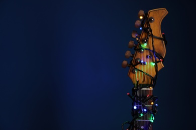 Guitar with festive lights on blue background, space for text. Christmas music Photo of Guitar with festive lights on blue background, space for text. Christmas music