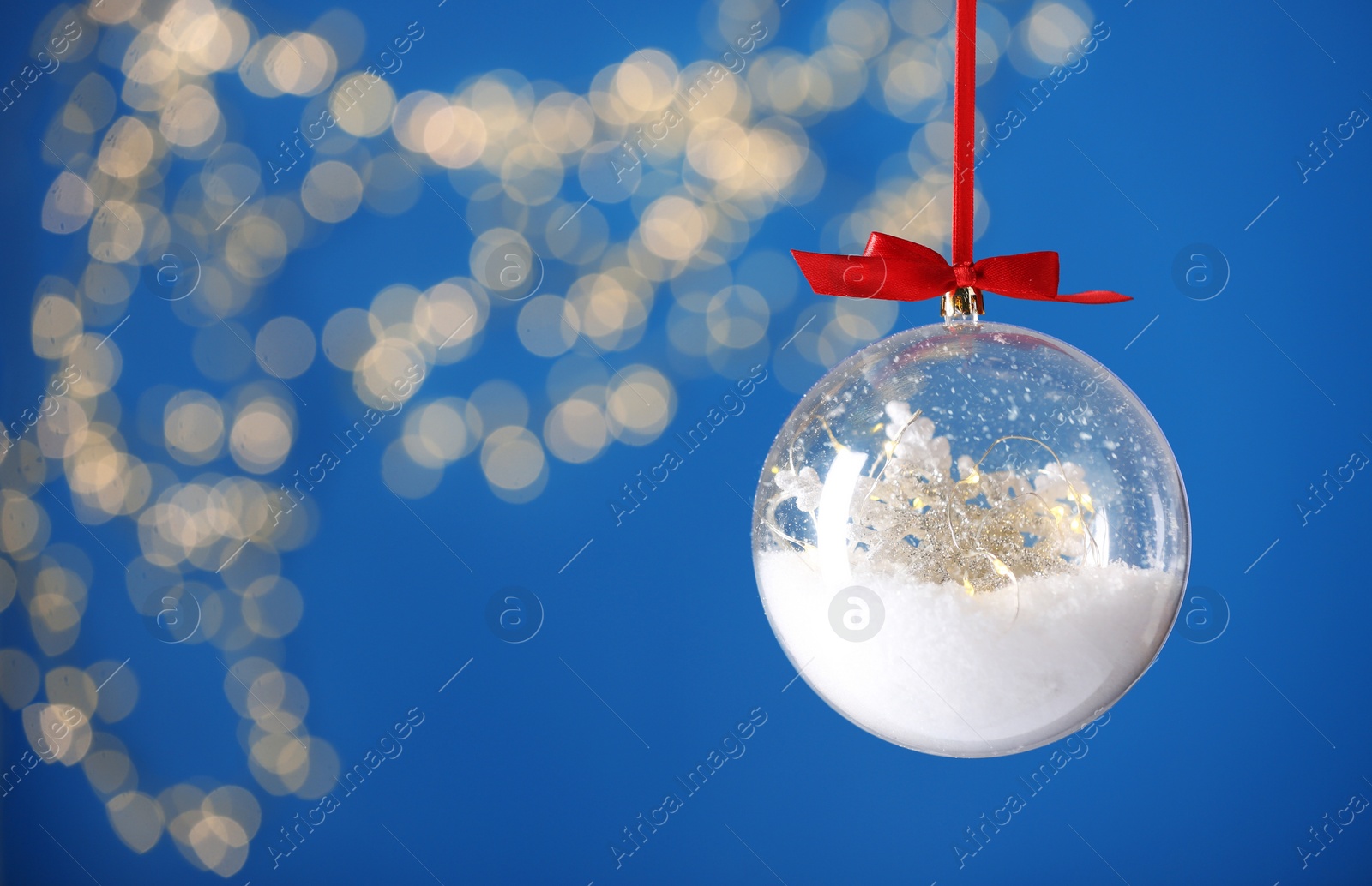 Decorative snow globe hanging against blurred festive lights, closeup. Space for text Photo of Decorative snow globe hanging against blurred festive lights, closeup. Space for text