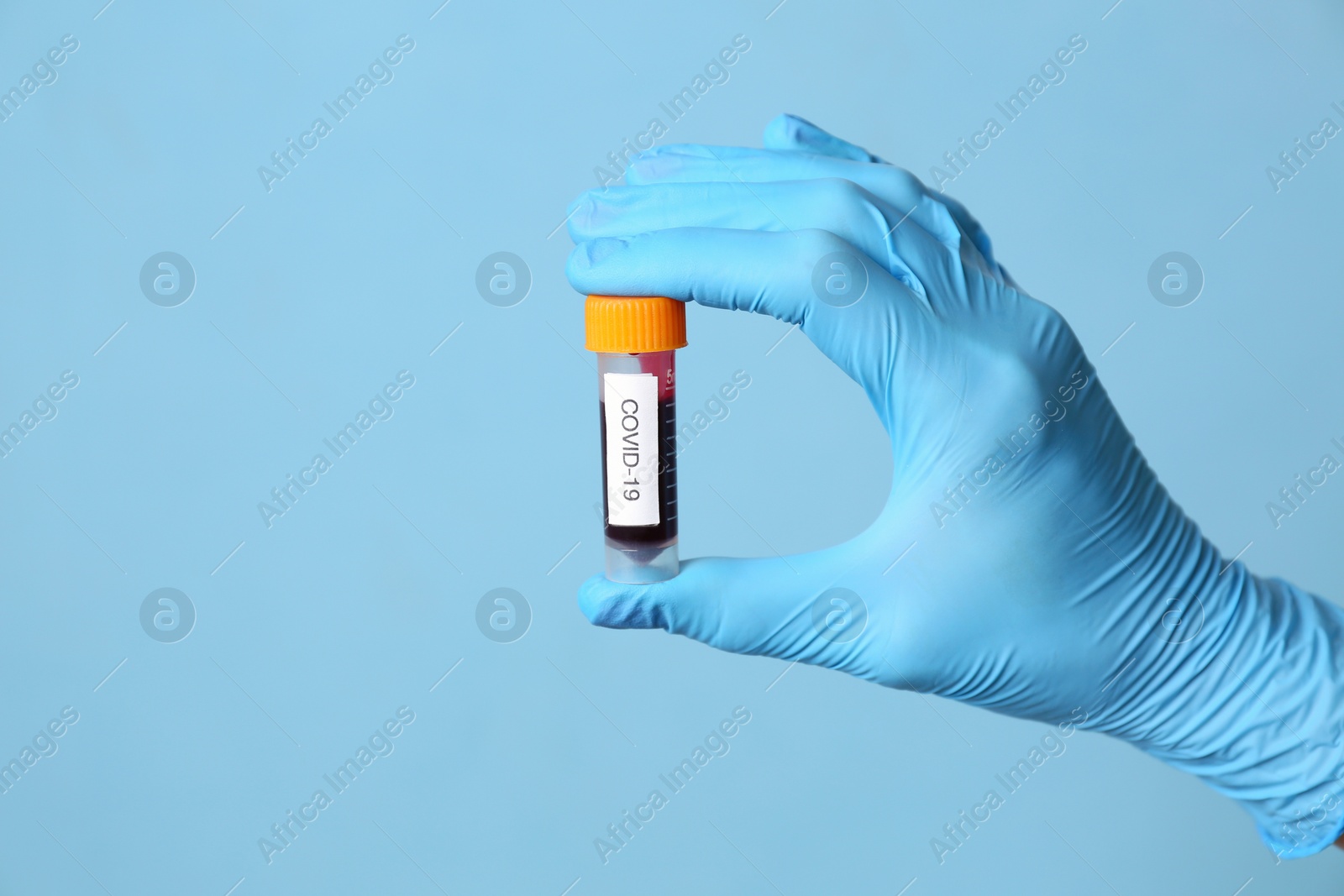 Scientist in protective gloves holding test tube with blood sample and label Covid-19 on light blue background, closeup. Space for text Photo of Scientist in protective gloves holding test tube with blood sample and label Covid-19 on light blue background, closeup. Space for text