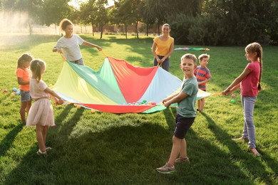 Group of children and teachers playing with rainbow playground parachute on green grass. Summer camp activity Photo of Group of children and teachers playing with rainbow playground parachute on green grass. Summer camp activity