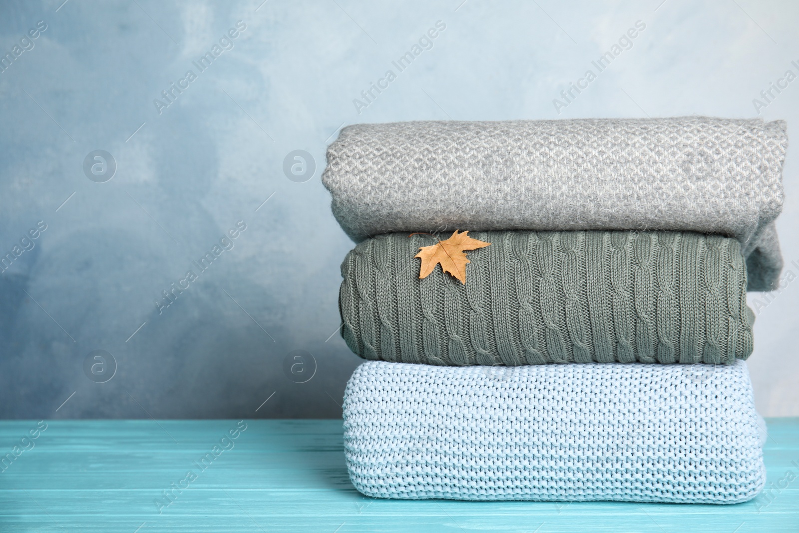 Stack of soft plaids and dry leaf on light blue wooden table. Space for text Photo of Stack of soft plaids and dry leaf on light blue wooden table. Space for text