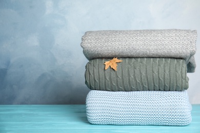 Stack of soft plaids and dry leaf on light blue wooden table. Space for text Photo of Stack of soft plaids and dry leaf on light blue wooden table. Space for text