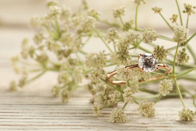 Beautiful engagement ring with gemstone and flowers on white wooden table, closeup. Space for text Photo of Beautiful engagement ring with gemstone and flowers on white wooden table, closeup. Space for text
