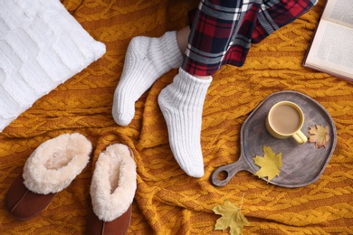 Photo of Woman relaxing with cup of hot winter drink on knitted plaid, top view. Cozy season