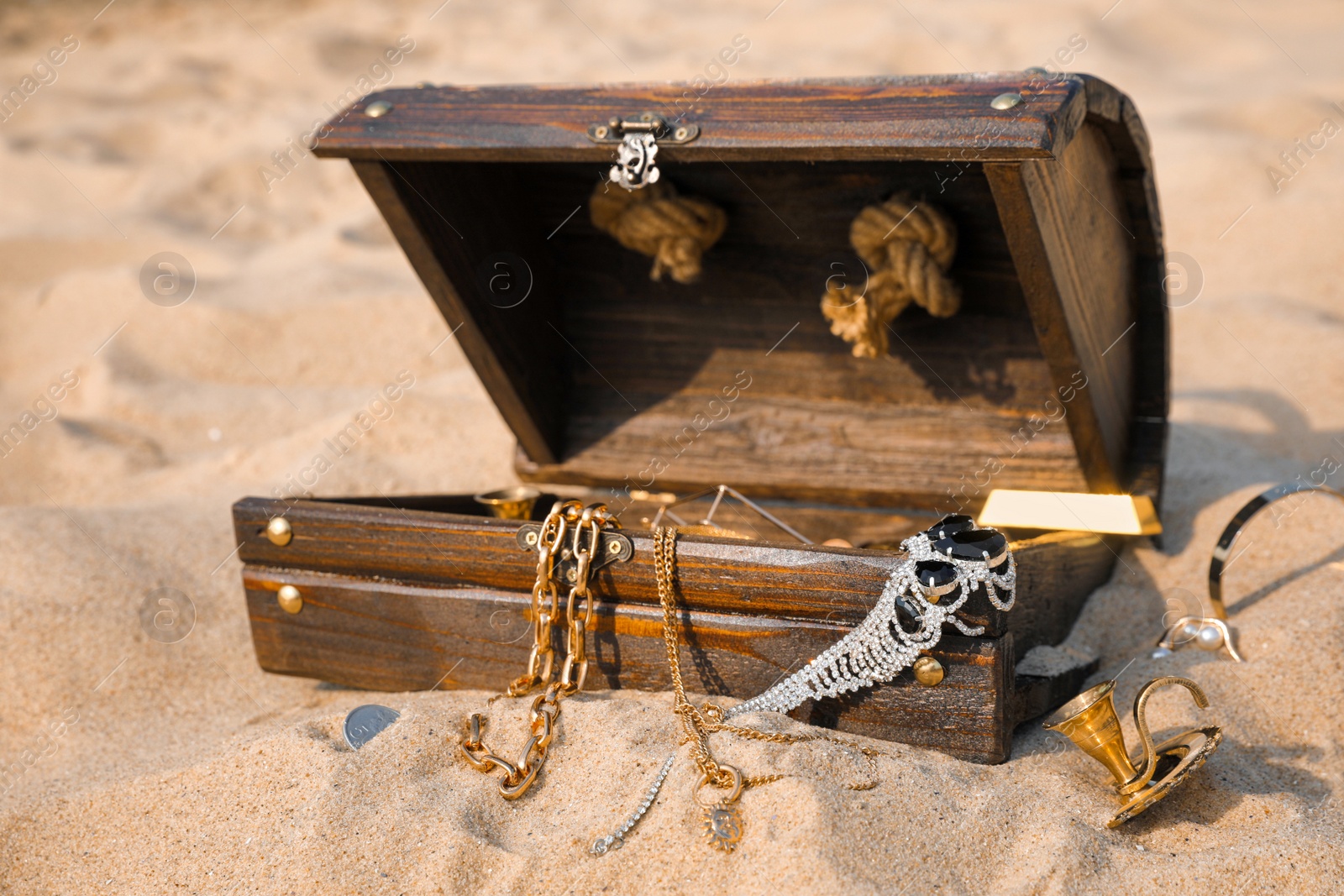 Open wooden chest with treasures on sand Photo of Open wooden chest with treasures on sand