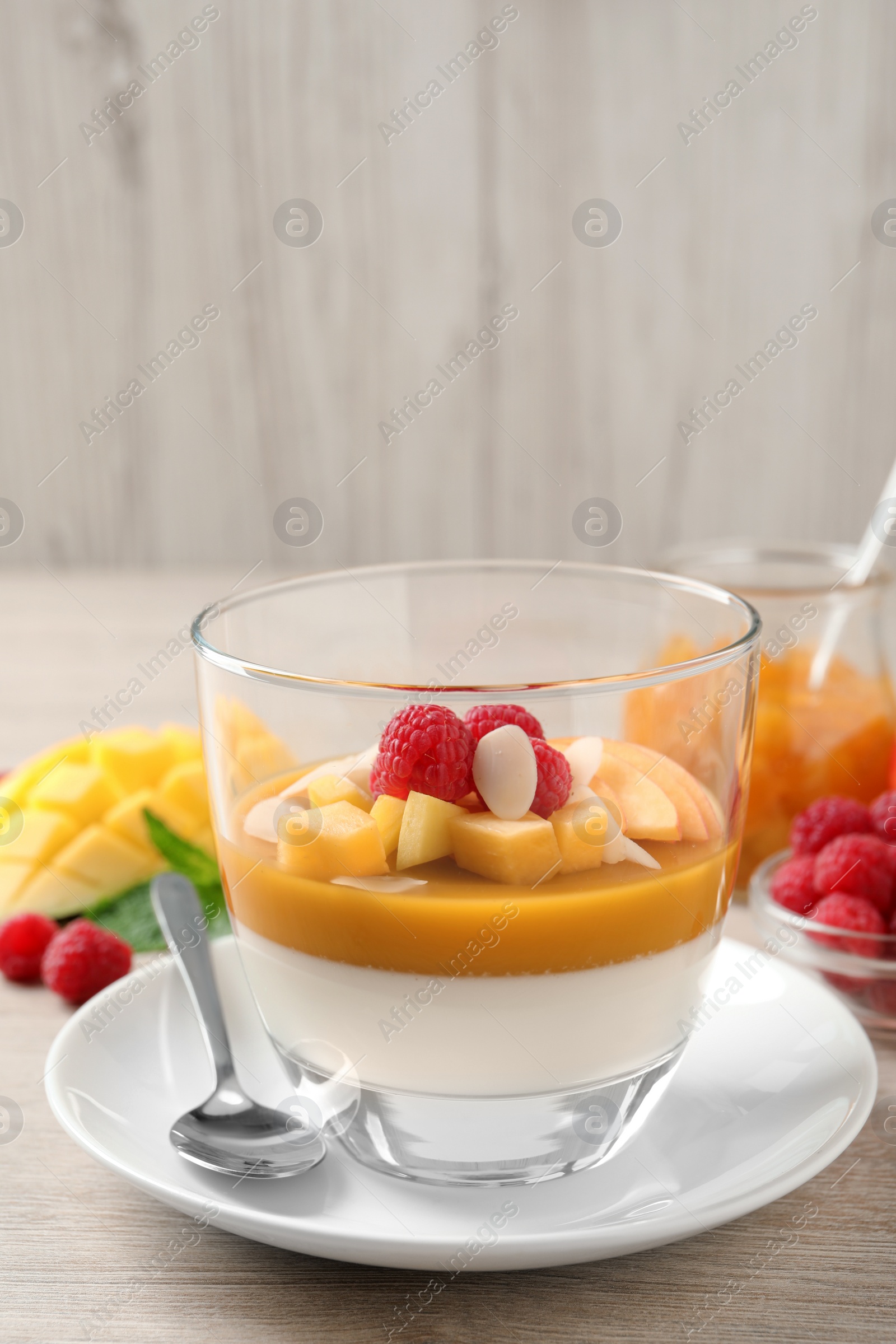 Delicious panna cotta with mango coulis, fresh fruit pieces and almond flakes on light wooden table Photo of Delicious panna cotta with mango coulis, fresh fruit pieces and almond flakes on light wooden table