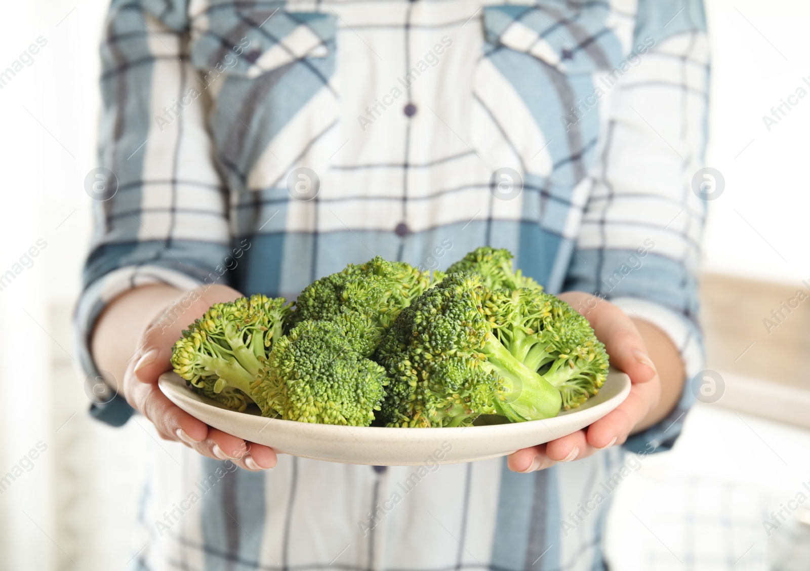 Woman holding plate with fresh green broccoli in kitchen, closeup Photo of Woman holding plate with fresh green broccoli in kitchen, closeup