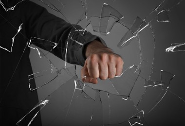 Man breaking window with fist on grey background, closeup Image of Man breaking window with fist on grey background, closeup