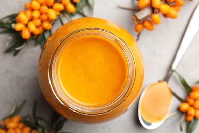 Delicious sea buckthorn jam and fresh berries on grey table, flat lay Photo of Delicious sea buckthorn jam and fresh berries on grey table, flat lay