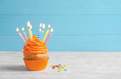 Delicious birthday cupcake with burning candles on table against color background Photo of Delicious birthday cupcake with burning candles on table against color background