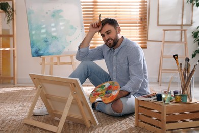 Young man painting on easel with brush in artist studio Photo of Young man painting on easel with brush in artist studio