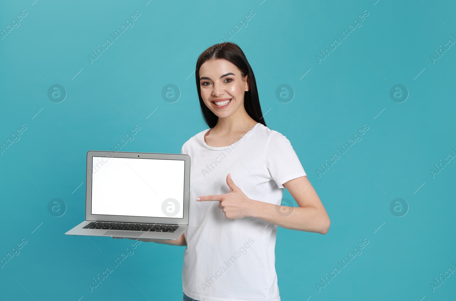 Young woman pointing at modern laptop with blank screen on light blue background Photo of Young woman pointing at modern laptop with blank screen on light blue background