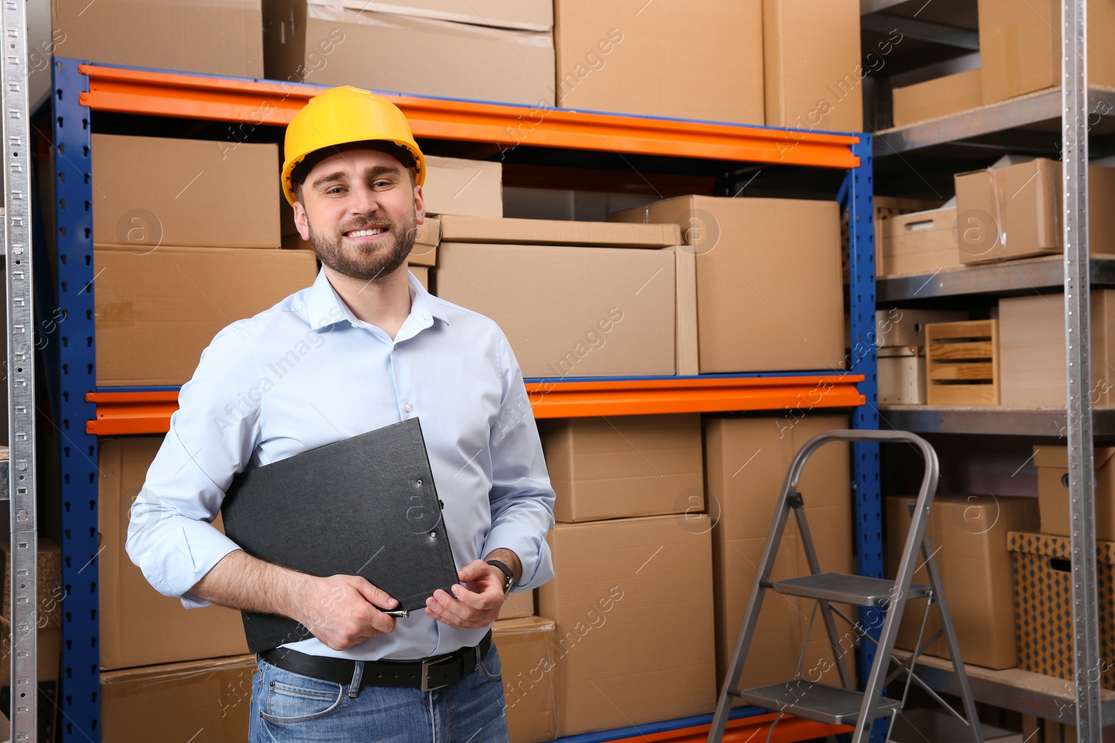 Young man with clipboard near rack of cardboard boxes at warehouse Photo of Young man with clipboard near rack of cardboard boxes at warehouse