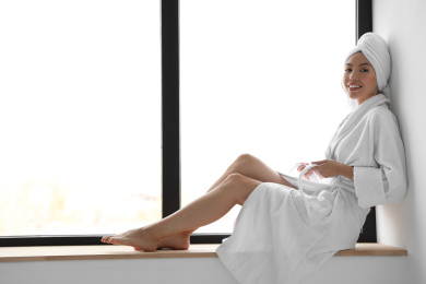 Photo of Young woman with towel wearing bathrobe near window