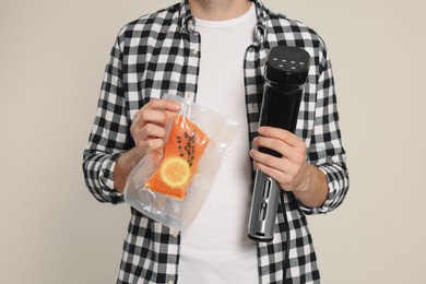 Man holding sous vide cooker and salmon in vacuum pack on beige background, closeup Photo of Man holding sous vide cooker and salmon in vacuum pack on beige background, closeup