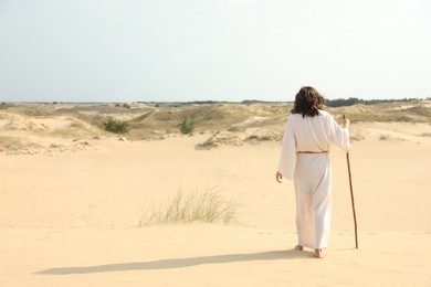 Jesus Christ walking with stick in desert, back view. Space for text Photo of Jesus Christ walking with stick in desert, back view. Space for text