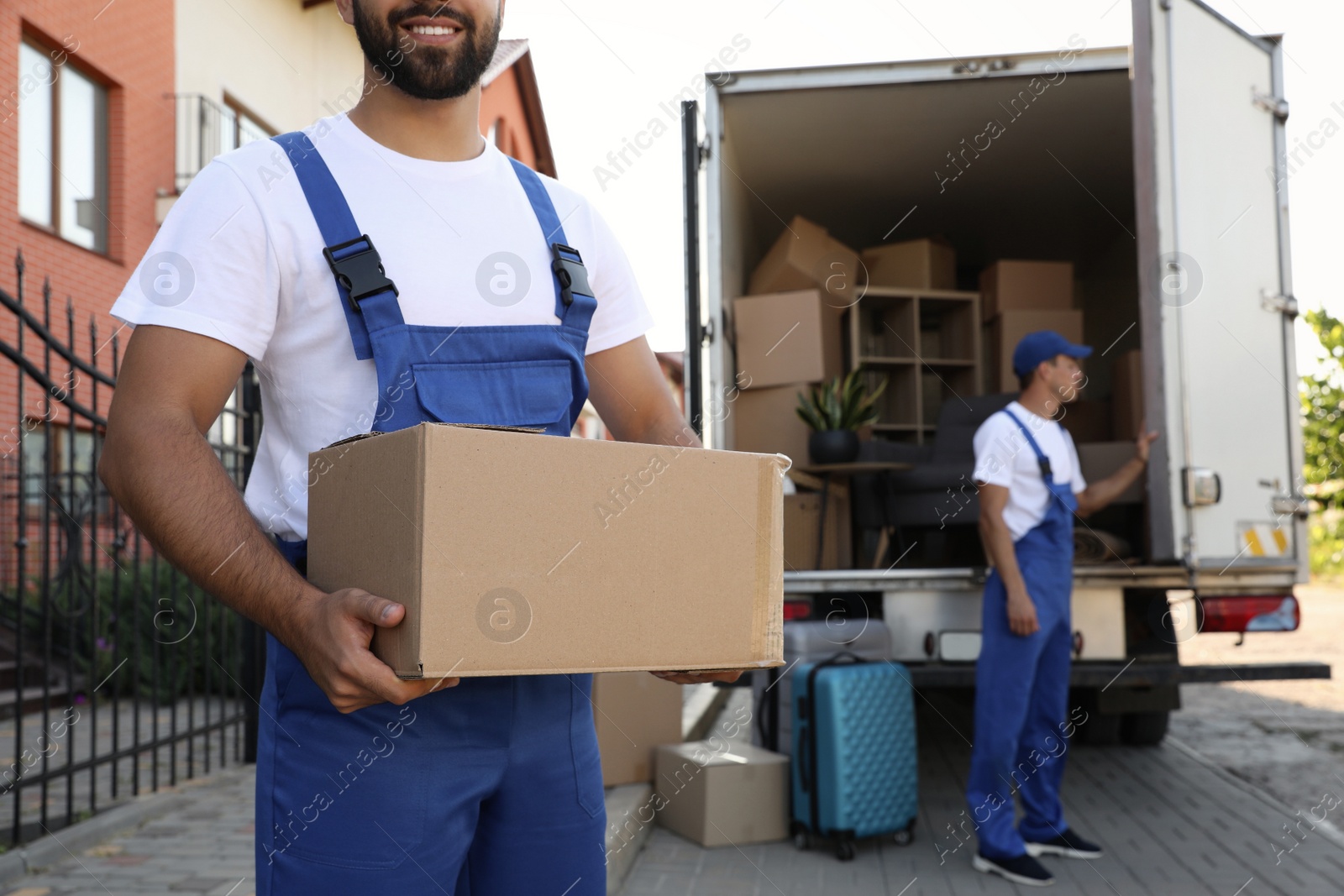 Photo of Workers unloading boxes from van outdoors, closeup. Moving service