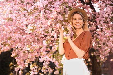 Young woman wearing stylish outfit near blossoming sakura in park. Fashionable spring look Photo of Young woman wearing stylish outfit near blossoming sakura in park. Fashionable spring look