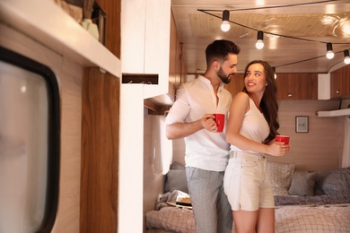 Happy young couple with cups in trailer. Camping vacation Photo of Happy young couple with cups in trailer. Camping vacation