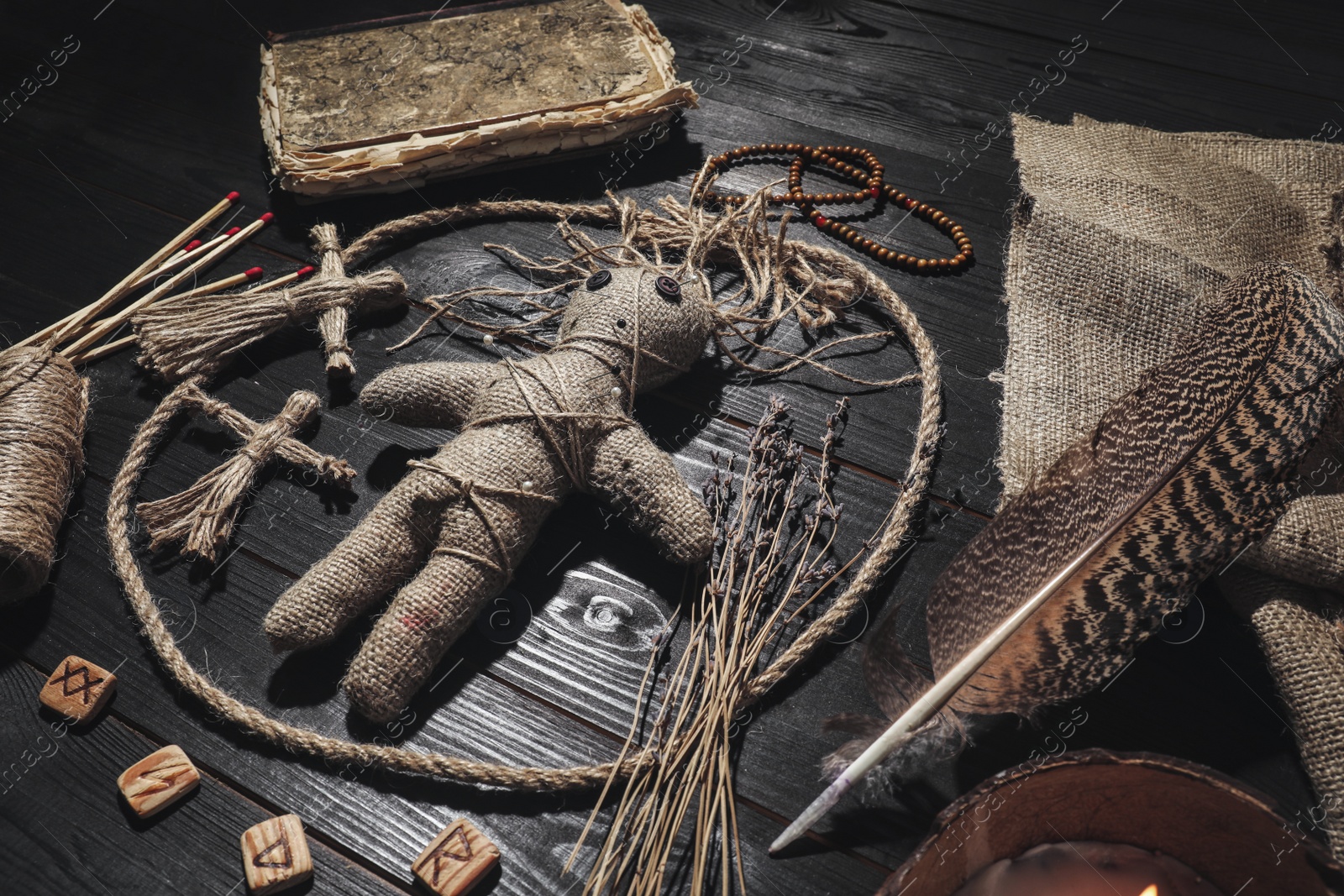 Female voodoo doll with pins surrounded by ceremonial items on black wooden background Photo of Female voodoo doll with pins surrounded by ceremonial items on black wooden background