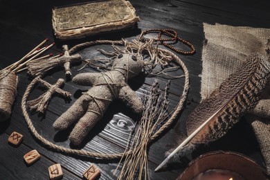 Female voodoo doll with pins surrounded by ceremonial items on black wooden background Photo of Female voodoo doll with pins surrounded by ceremonial items on black wooden background