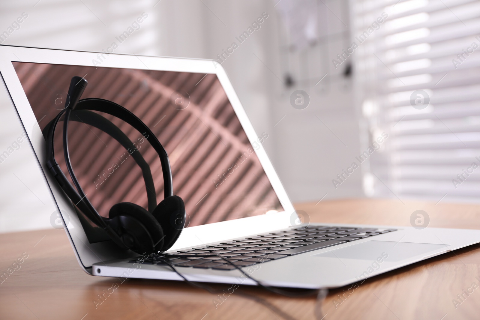 Modern laptop with headset on wooden table in office, space for text. Hotline service Photo of Modern laptop with headset on wooden table in office, space for text. Hotline service