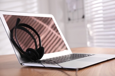 Modern laptop with headset on wooden table in office, space for text. Hotline service Photo of Modern laptop with headset on wooden table in office, space for text. Hotline service