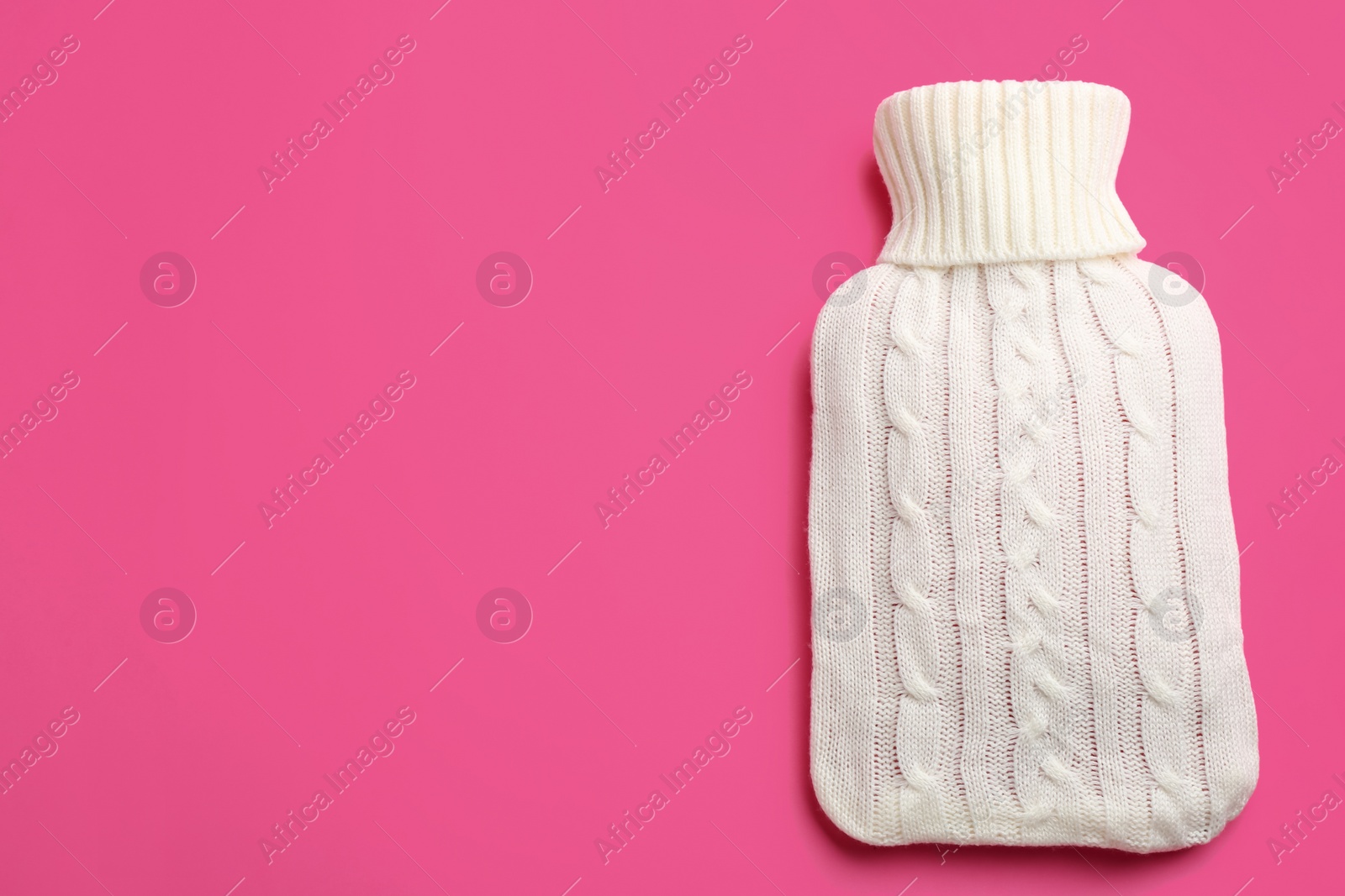 Photo of Hot water bottle with knitted cover on pink background, top view. Space for text