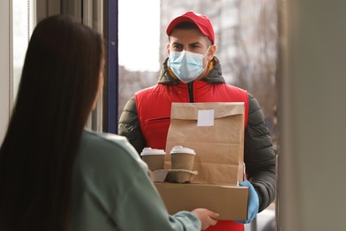 Courier in medical mask giving to woman her order at doorway. Delivery service during Covid-19 quarantine Photo of Courier in medical mask giving to woman her order at doorway. Delivery service during Covid-19 quarantine