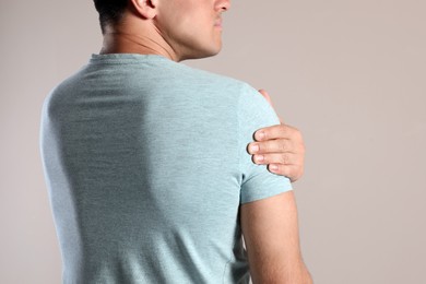 Man suffering from shoulder pain on beige background, closeup Photo of Man suffering from shoulder pain on beige background, closeup