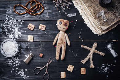 Voodoo doll with pins surrounded by ceremonial items on black wooden table, flat lay Photo of Voodoo doll with pins surrounded by ceremonial items on black wooden table, flat lay