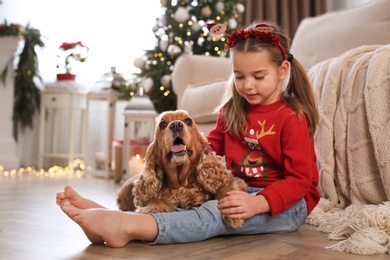 Photo of Cute little girl with English Cocker Spaniel in room decorated for Christmas