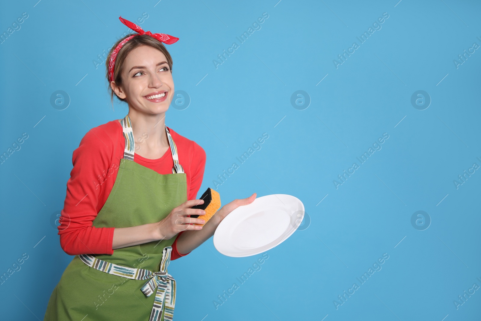 Young housewife with plate and sponge on light blue background. Space for text Photo of Young housewife with plate and sponge on light blue background. Space for text
