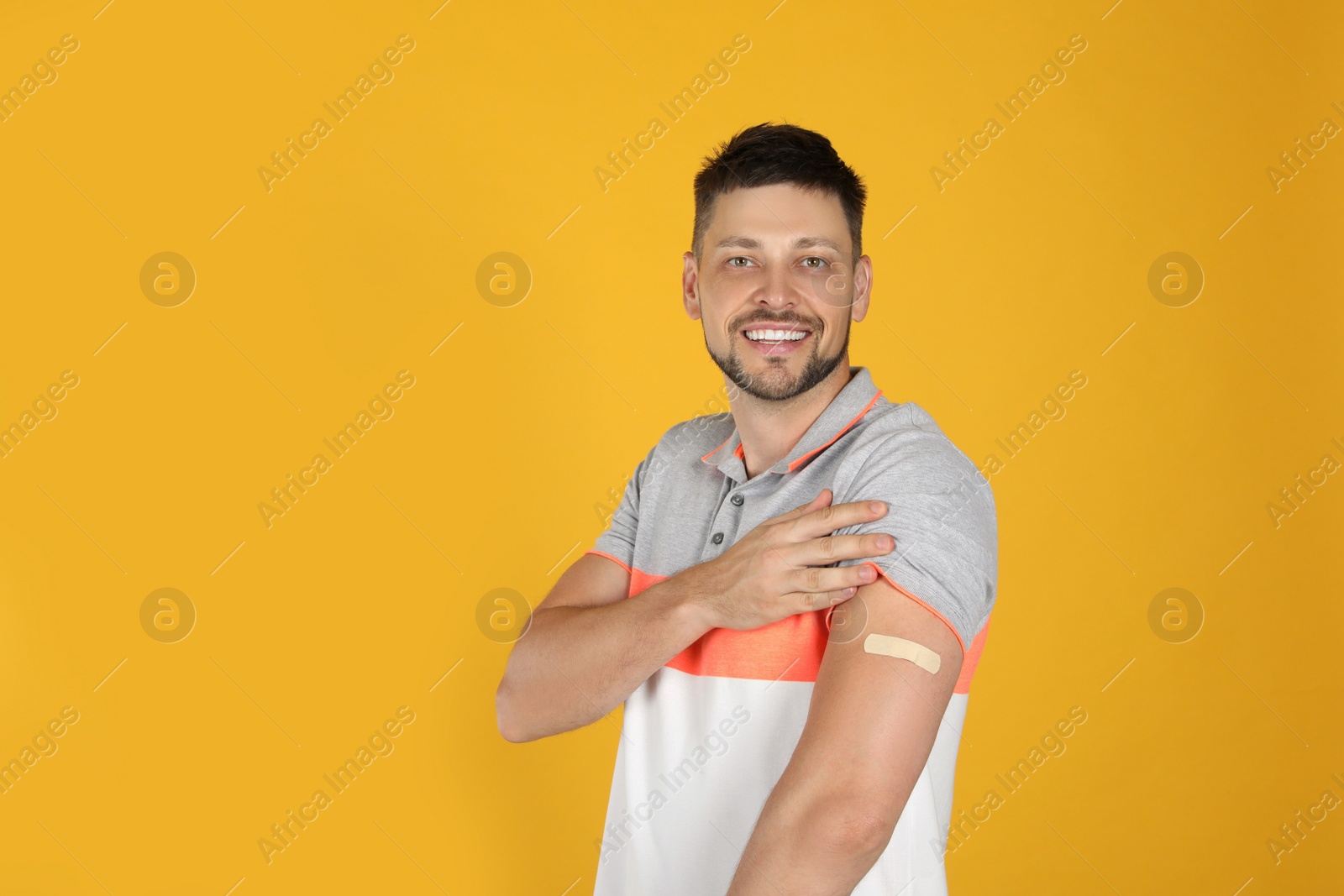 Vaccinated man showing medical plaster on his arm against yellow background. Space for text Photo of Vaccinated man showing medical plaster on his arm against yellow background. Space for text