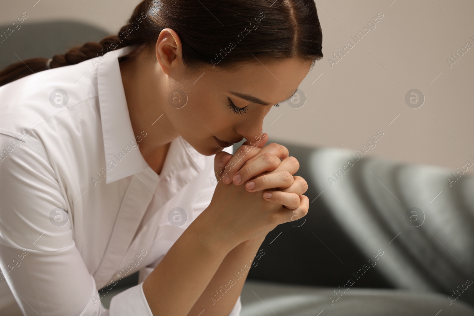 Photo of Religious young woman with clasped hands praying indoors
