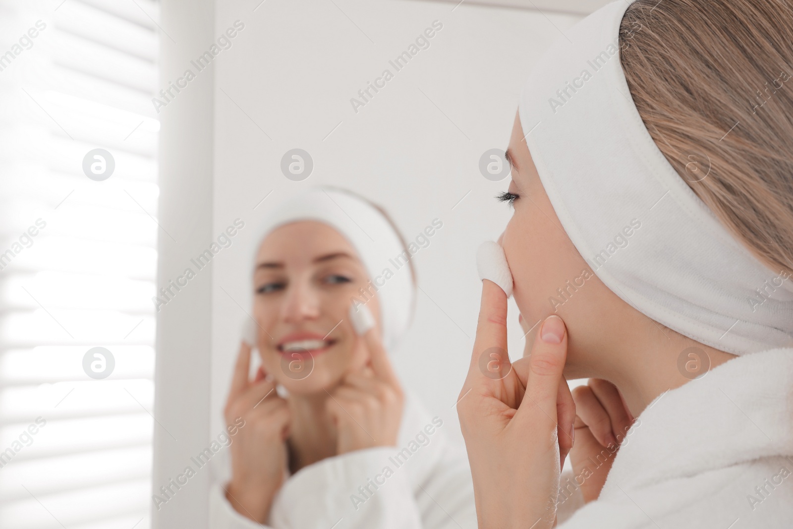 Woman using silkworm cocoons in skin care routine near mirror at home Photo of Woman using silkworm cocoons in skin care routine near mirror at home