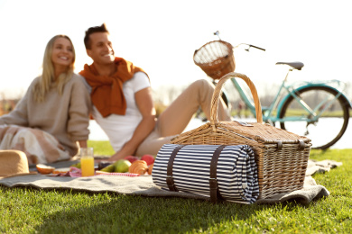 Happy young couple having picnic outdoors, focus on wicker basket Photo of Happy young couple having picnic outdoors, focus on wicker basket
