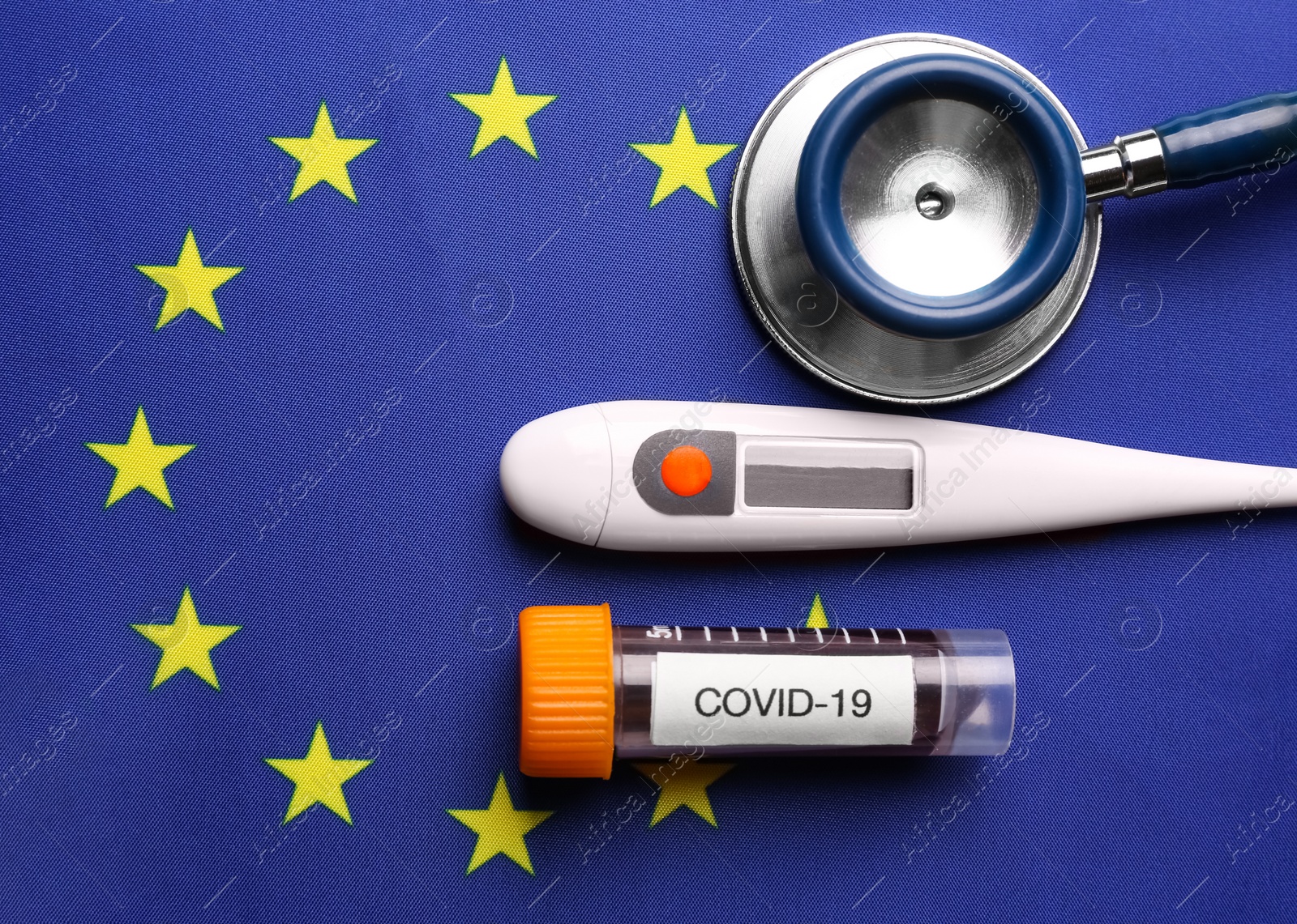 Test tube with blood sample, thermometer and stethoscope on European Union flag background, flat lay. Coronavirus outbreak Photo of Test tube with blood sample, thermometer and stethoscope on European Union flag background, flat lay. Coronavirus outbreak