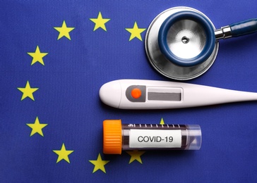 Test tube with blood sample, thermometer and stethoscope on European Union flag background, flat lay. Coronavirus outbreak Photo of Test tube with blood sample, thermometer and stethoscope on European Union flag background, flat lay. Coronavirus outbreak
