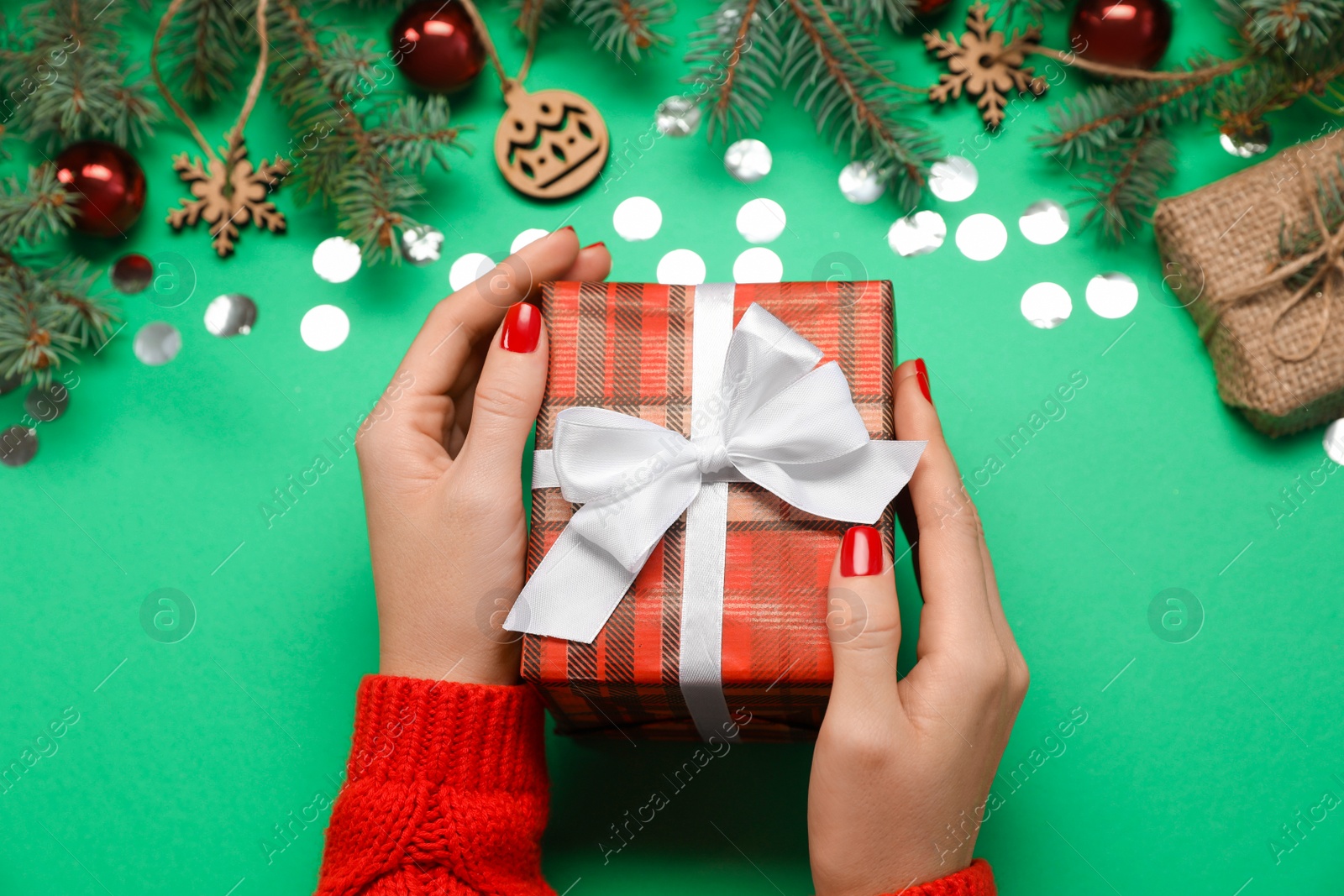 Woman holding gift box near fir tree branches with Christmas decor on green background, above view Photo of Woman holding gift box near fir tree branches with Christmas decor on green background, above view