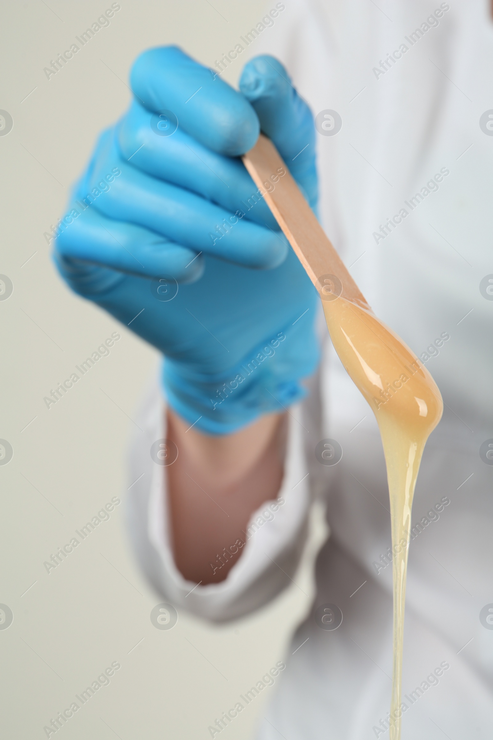 Woman in gloves holding spatula with hot depilatory wax, closeup Photo of Woman in gloves holding spatula with hot depilatory wax, closeup