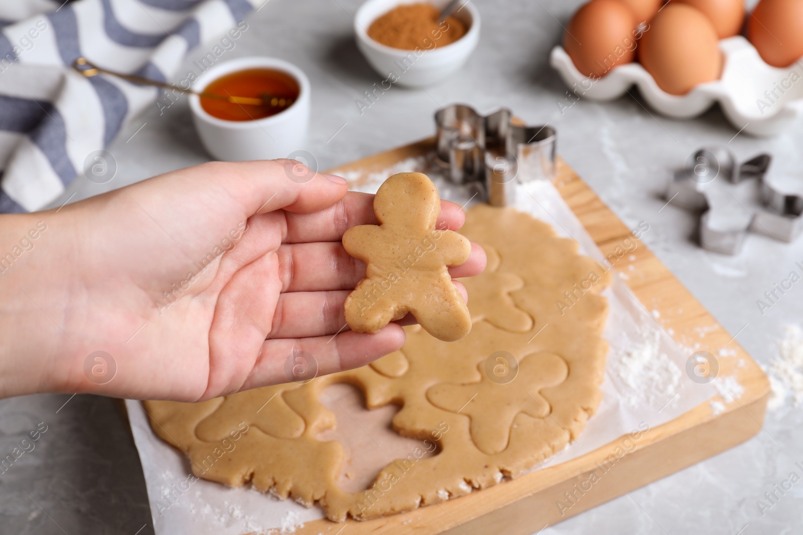 Making homemade Christmas cookies. Woman holding gingerbread man above light grey marble table, closeup Photo of Making homemade Christmas cookies. Woman holding gingerbread man above light grey marble table, closeup