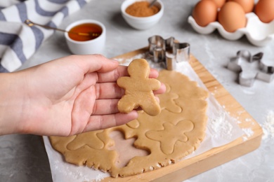 Making homemade Christmas cookies. Woman holding gingerbread man above light grey marble table, closeup Photo of Making homemade Christmas cookies. Woman holding gingerbread man above light grey marble table, closeup