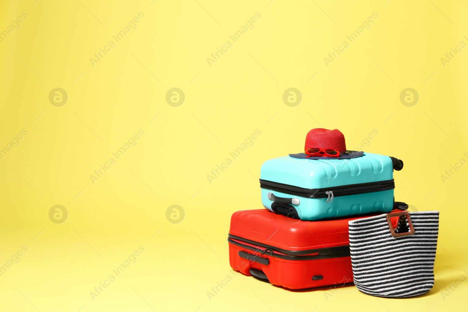 Stylish suitcases with hat and bag on yellow background. Space for text Photo of Stylish suitcases with hat and bag on yellow background. Space for text
