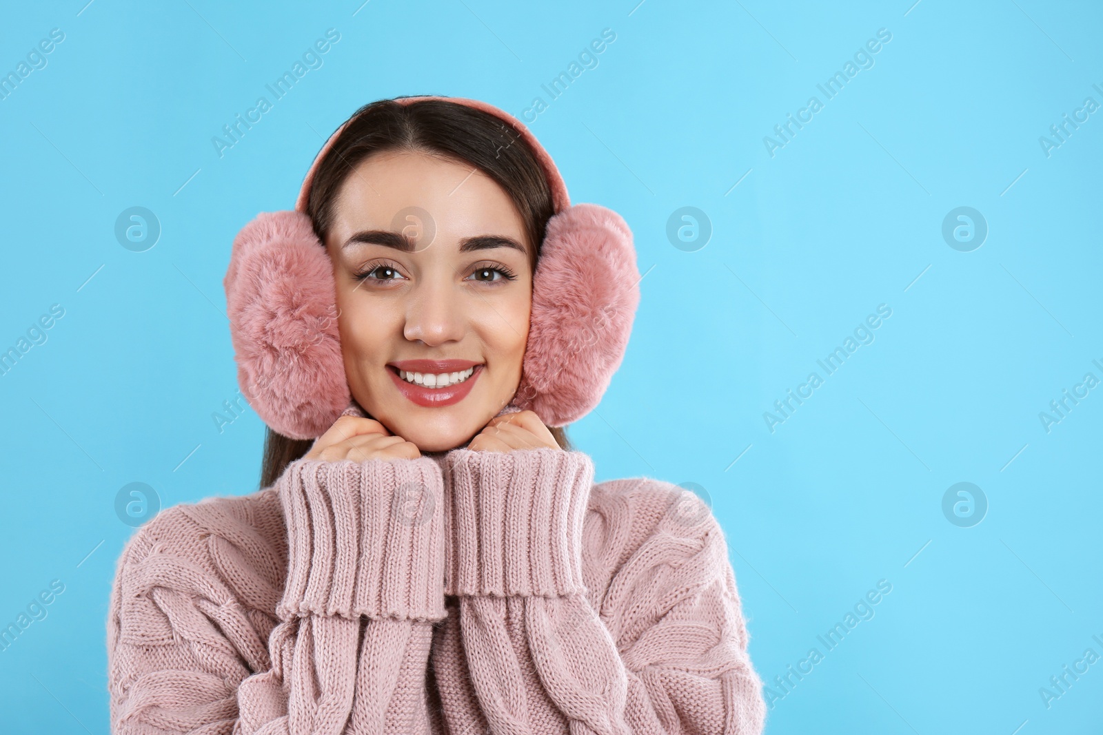Beautiful young woman wearing earmuffs on light blue background. Space for text Photo of Beautiful young woman wearing earmuffs on light blue background. Space for text