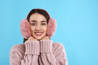 Beautiful young woman wearing earmuffs on light blue background. Space for text Photo of Beautiful young woman wearing earmuffs on light blue background. Space for text
