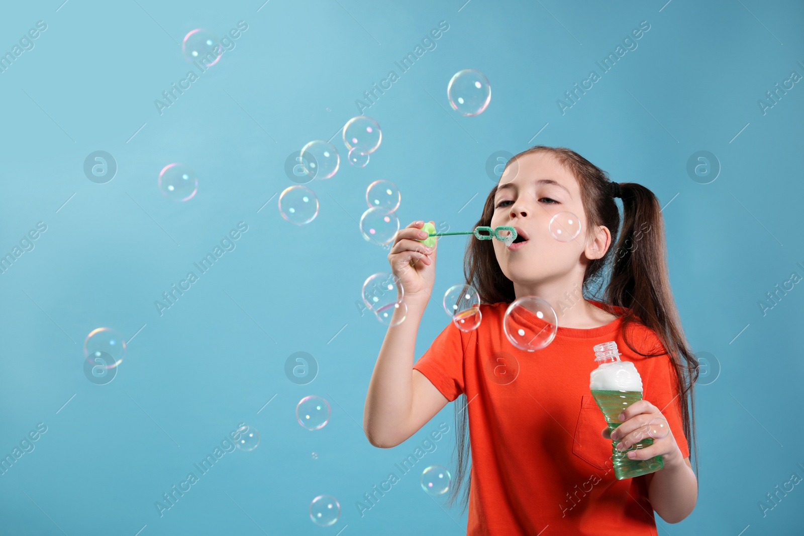 Little girl blowing soap bubbles on light blue background, space for text Photo of Little girl blowing soap bubbles on light blue background, space for text